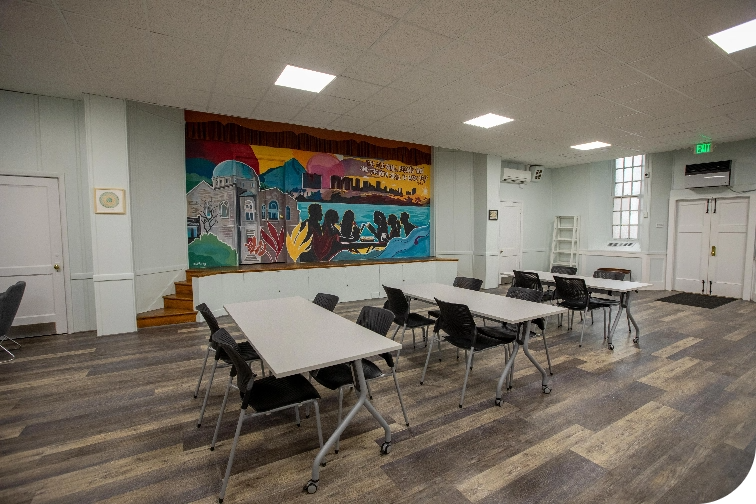 View of the beit midrash (classroom) with movable tables, mural featuring the building, and stage