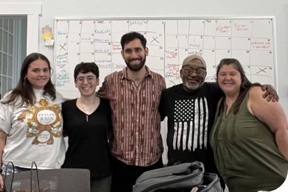 Five people stand shoulder to shoulder in front of a white board with a calendar grid. 