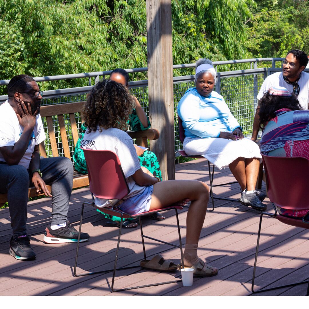 Six Jews of Color seated on an outdoor deck with stripes of sunshine and shadow