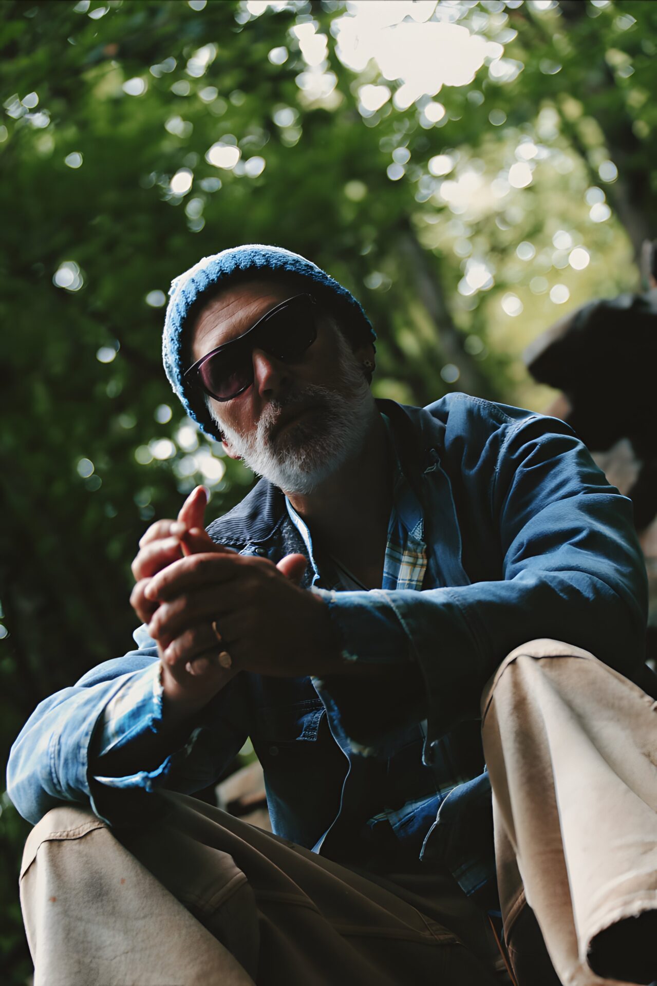 Matisyahu, seated in the woods, wearing sunglasses and a knit cap