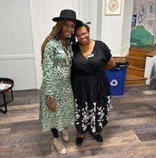 Two women wearing long dresses smile for a photo together.