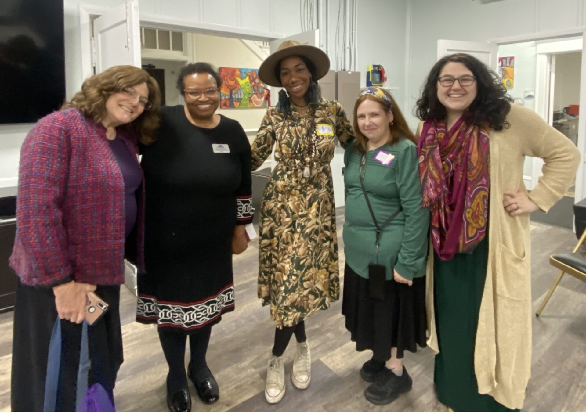 five women of different races and religions stand together with their arms around each other.