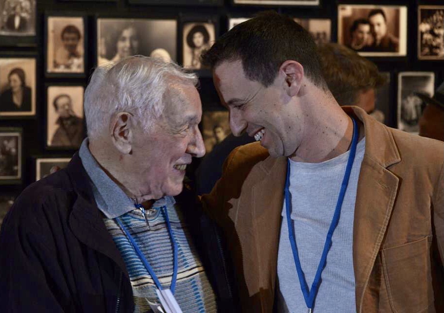 David and Avi Wisnia smile at one another, foreheads nearly touching. Black and white photos adorn the wall behind them.