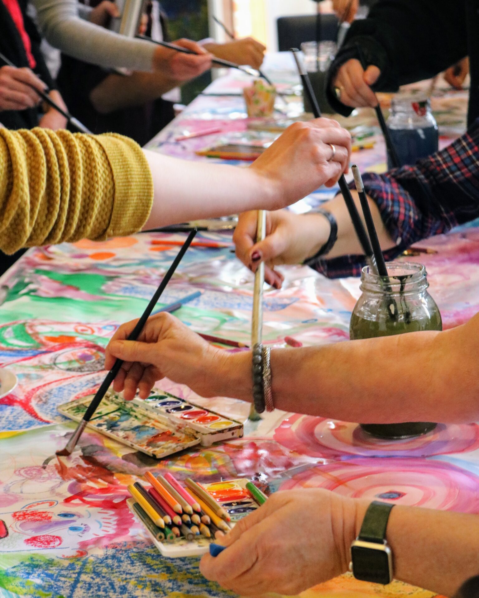 Close up of multiple people's hands working with long paint brushes and water colors